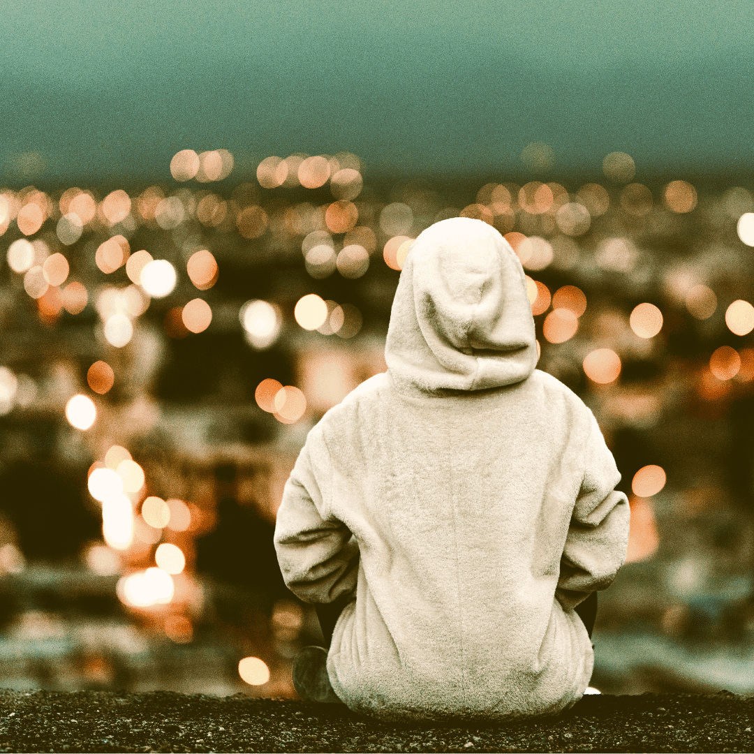 Back of a teenager in a hoodie on a wall looking at a cityscape
